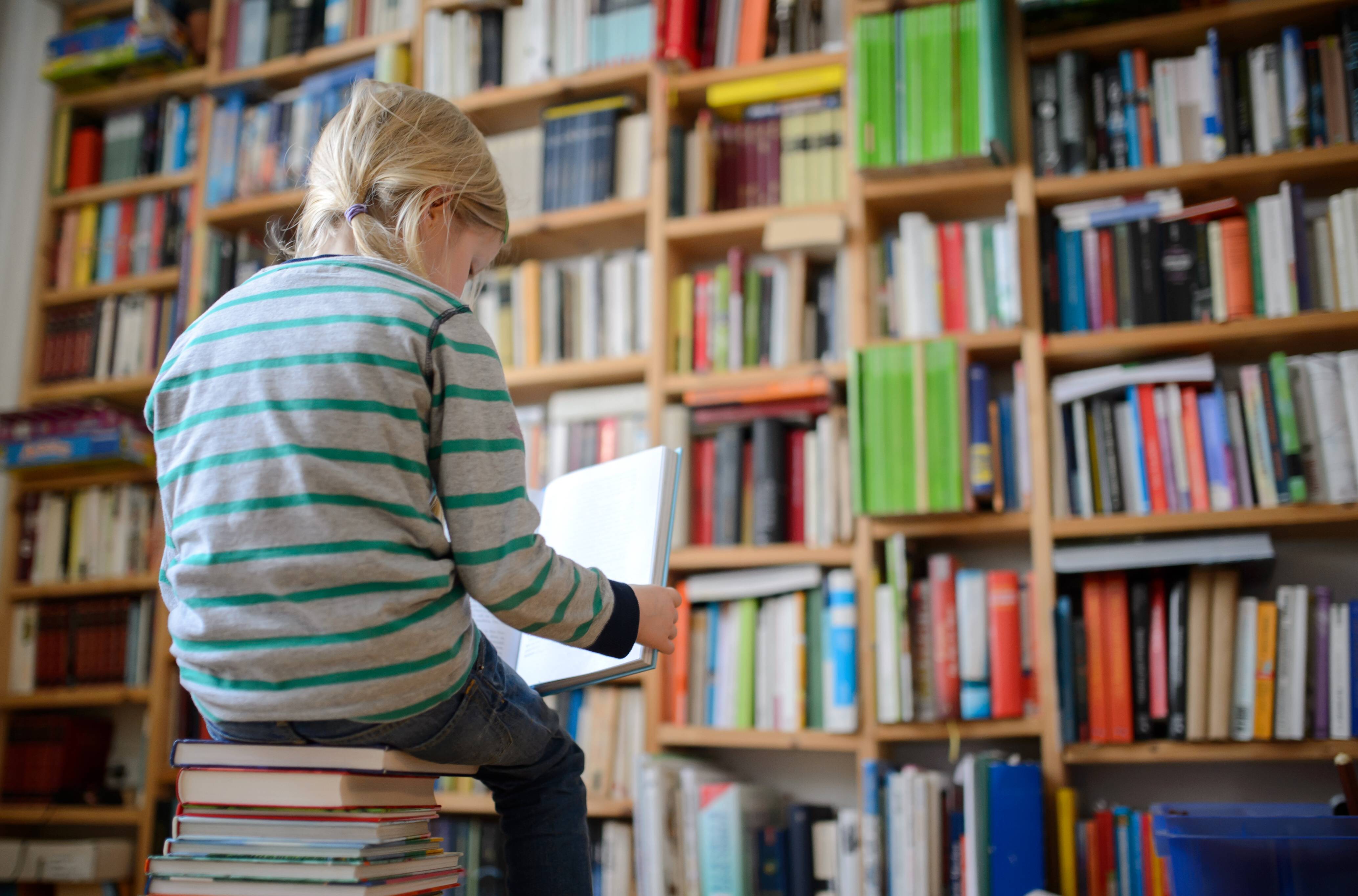 Ein Kind sitzt auf einem Buchstapel und liest ein Buch