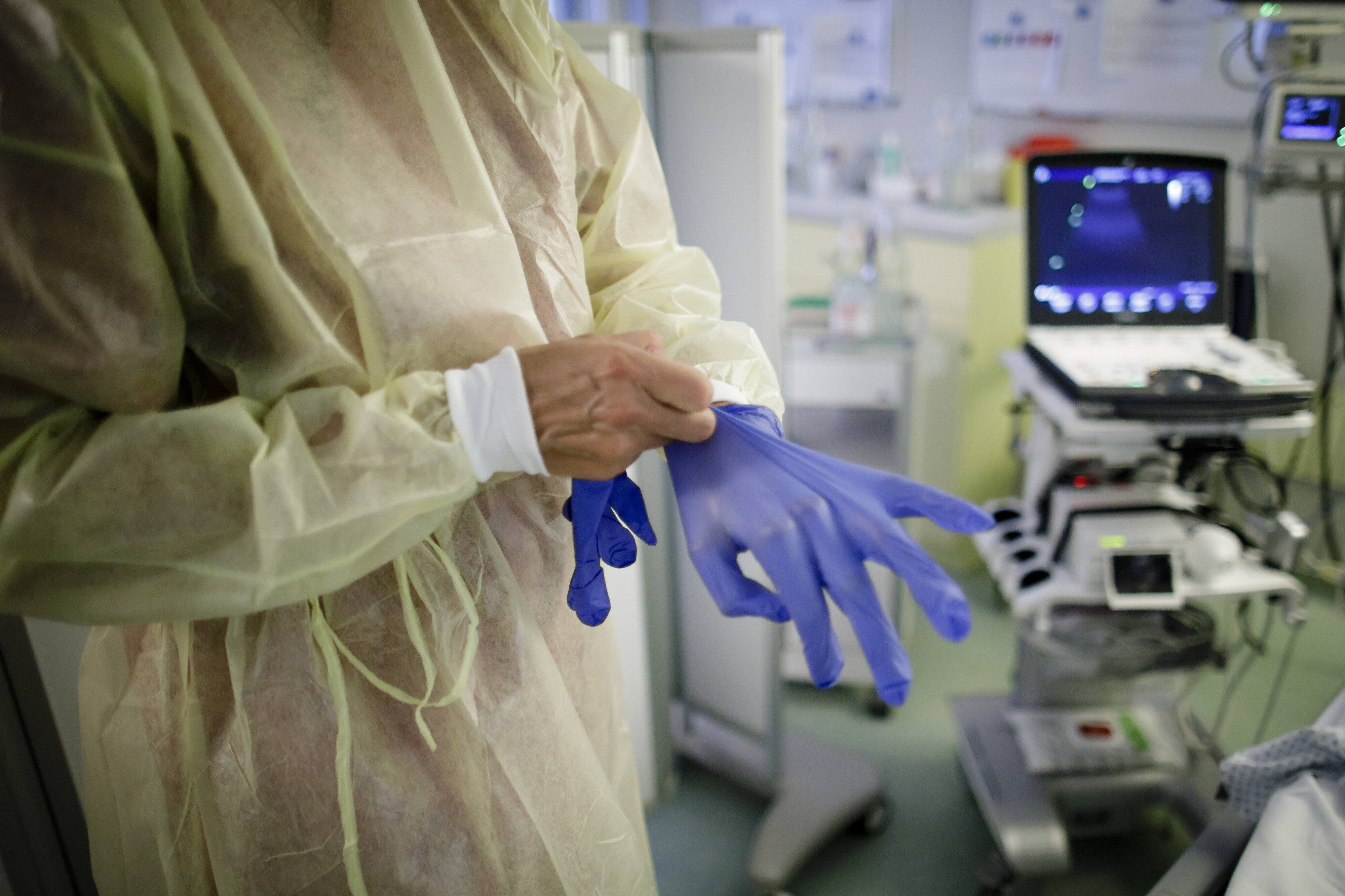 Eine Aerztin zieht sich blaue Handschuhe in einer Intensivstation an.