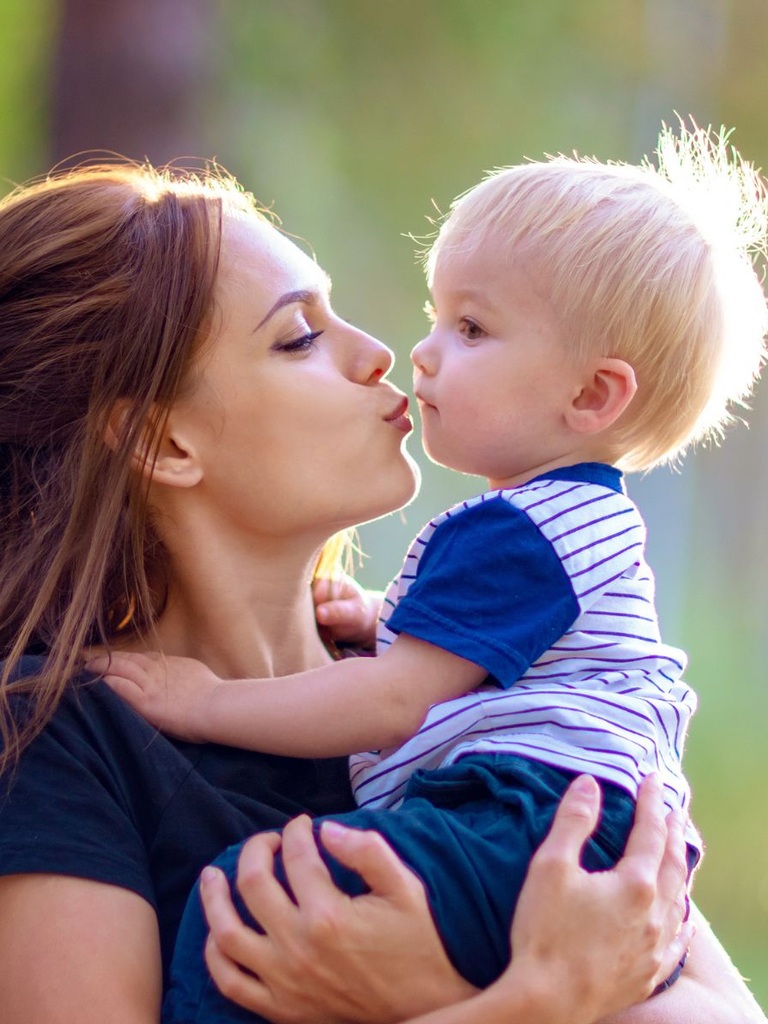 Eine junge Mutter will ihrem kleinen Sohn einen Kuss geben.